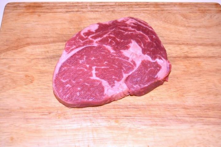 Ribeye Steak in Air Fryer-Ribeye Steak on the Chopping Board Thick-cut marbled raw ribeye steak at room temperature on a wooden chopping board.
