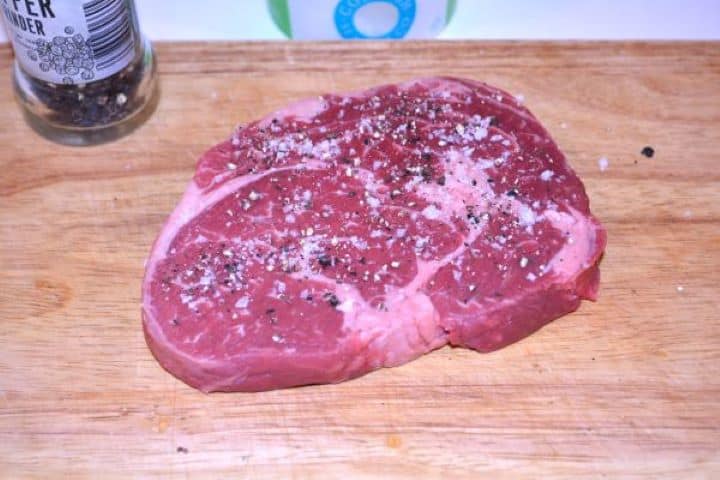 Ribeye Steak in Air Fryer-Seasoned Ribeye Steak on the Chopping Board Raw ribeye steak seasoned with sea salt flakes, freshly cracked black pepper, and garlic powder on a wooden board.