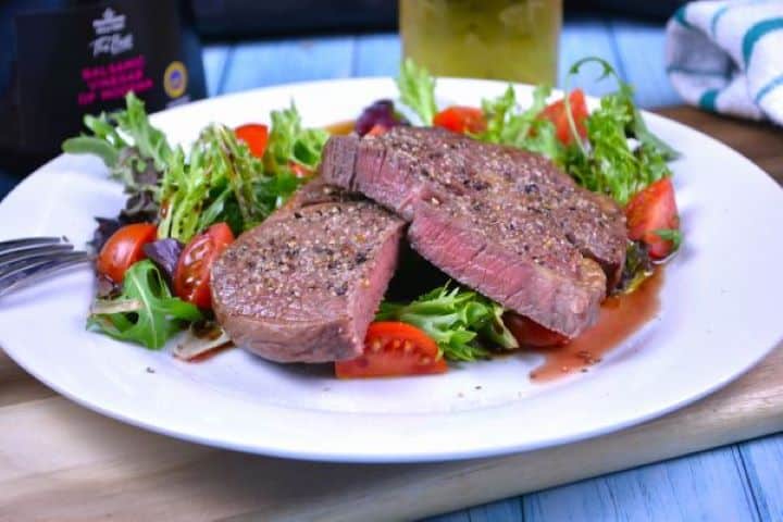 Ribeye Steak in Air Fryer-Served on Plate With Lettuce and Tomatoes Salad Juicy ribeye steak in air fryer served on white plate with lettuce and tomatoes salad.