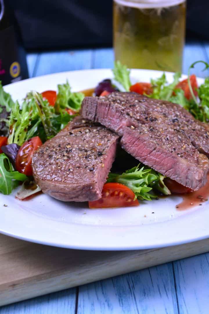 Juicy air fryer ribeye steak served on a white plate with fresh cherry tomato salad and balsamic dressing.