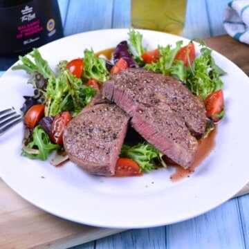 Juicy air fryer ribeye steak served on a white plate with fresh cherry tomato salad and balsamic dressing.