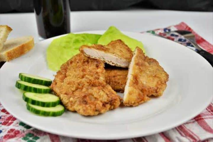 Turkey Schnitzel Recipe-Served on Plate With Cucumber and Lettuce Overhead view of homemade turkey schnitzels arranged on a serving platter with sliced cucumbers and green salad.