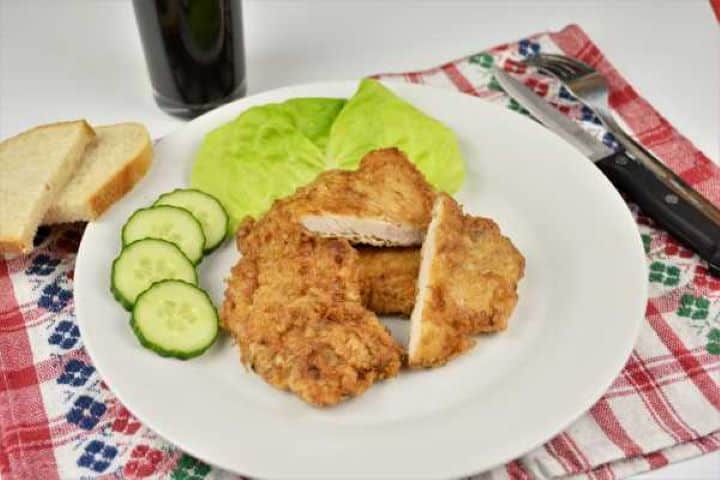 Turkey Schnitzel Recipe-Served on Plate With Cucumber and Lettuce Juicy turkey schnitzel cutlet served hot with sliced cucumber, fresh lettuce, and white bread slices.