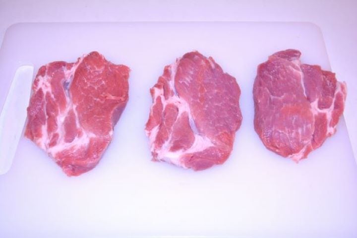 Pork Steak in Air Fryer-Pork Shoulder Steaks on the Chopping Board Raw sliced pork shoulder steaks on a white cutting board showing natural fat marbling.