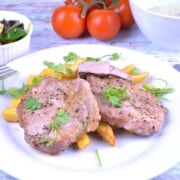Juicy air fryer pork steak served on a white plate with french fries, garlic sauce, and fresh salad.