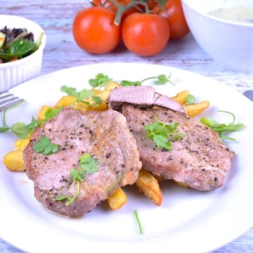 Juicy air fryer pork steak served on a white plate with french fries, garlic sauce, and fresh salad.