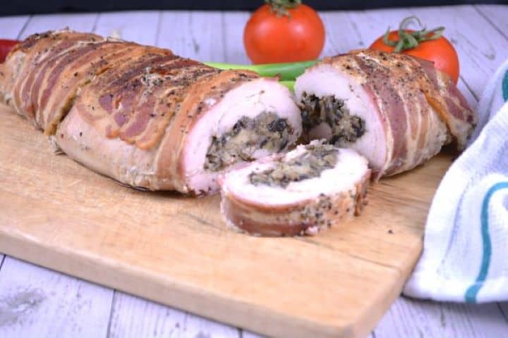 Thick pinwheel slices of bacon-wrapped stuffed turkey tenderloin served warm on a wooden carving board.
