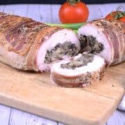 Sliced bacon wrapped stuffed turkey tenderloin pinwheels showing melted cheddar and mushroom filling on a wooden board.
