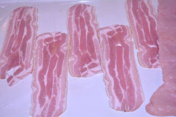 Stuffed Turkey Tenderloin Recipe-Smoked Bacon Slices on the Wrapping Foil Overlapping strips of smoked bacon laid flat across clear plastic wrap on a countertop.