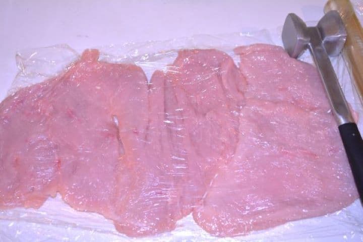 Stuffed Turkey Tenderloin Recipe-Tenderized Turkey Breast on the Table Pounding butterflied turkey tenderloin under plastic cling film to an even half-inch thickness with a meat mallet.