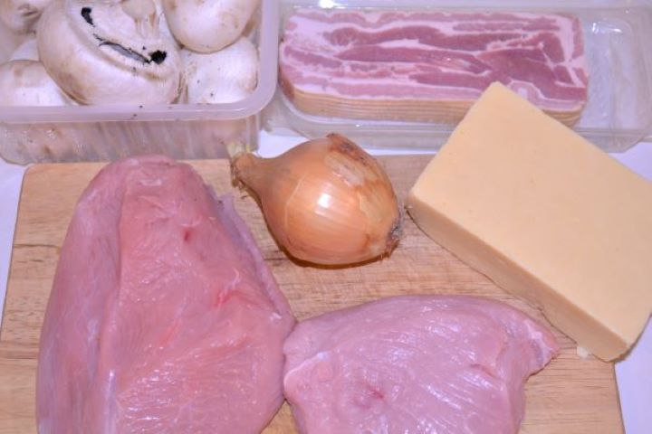 Stuffed Turkey Tenderloin Recipe-Turkey Breast, Onion, Cheddar Cheese, Mushrooms and Smoked Bacon Raw turkey tenderloin, smoked bacon slices, white mushrooms, yellow onion, and cheddar cheese on a kitchen table.