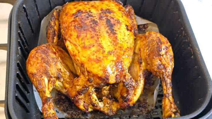Ready Flipping a partially cooked whole chicken breast side up using tongs in an air fryer.