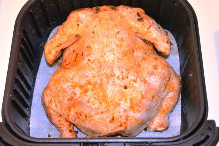 Chicken in Basket Seasoned raw whole chicken placed breast side down inside a square Cosori XL air fryer basket.