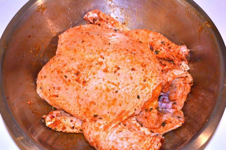 Seasoning Rubbing a raw whole chicken with a spice mixture and sunflower oil in a bowl.