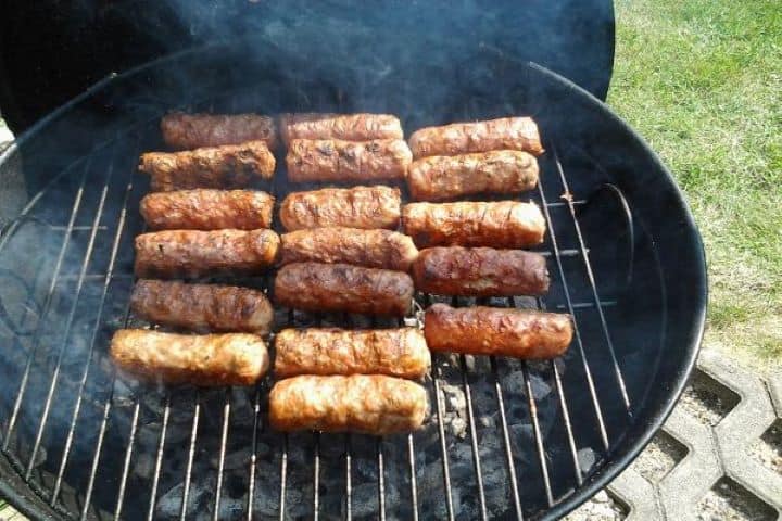 Grill Authentic Romanian mici sizzling directly over hot coals on an outdoor barbecue grill.
