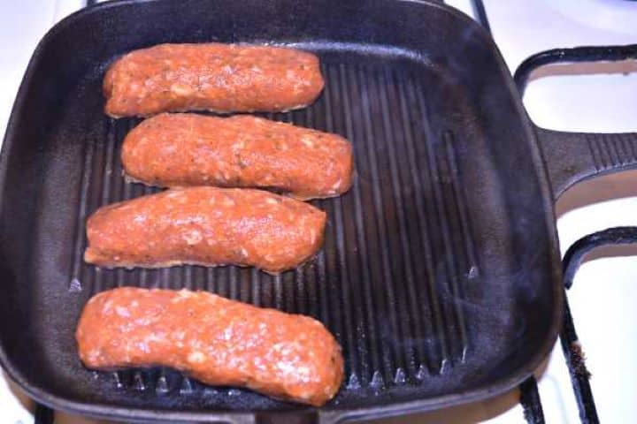 Frying Raw skinless sausage rolls searing in a hot cast-iron skillet on the stovetop.