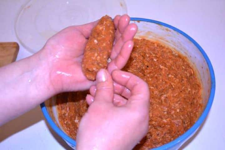 Rolling Shaping a 60-gram casing-free sausage cylinder by hand using wet palms over a mixing bowl.