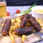 Juicy homemade skinless sausages (Romanian mici) served on a wooden board with golden French fries and yellow mustard.