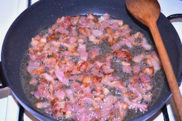 Fried Bacon Golden crispy fried bacon pieces sizzling in rendered fat in a skillet.