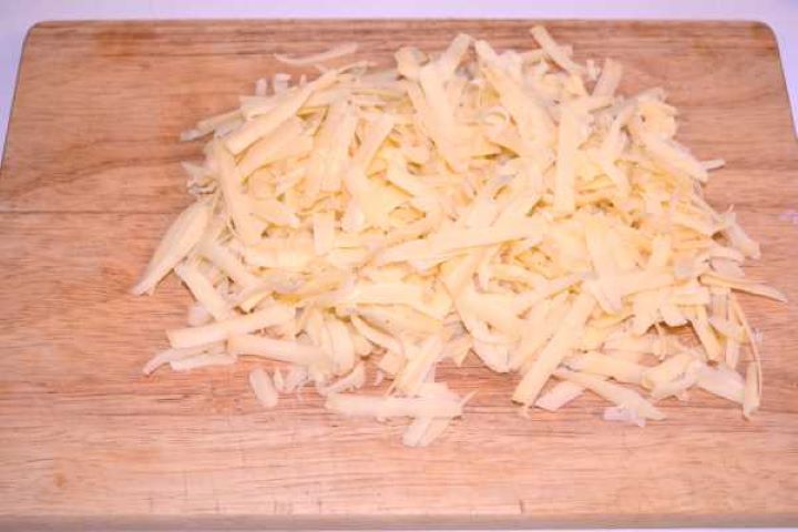 Grated Cheddar Freshly grated sharp cheddar cheese piled on a wooden chopping board.