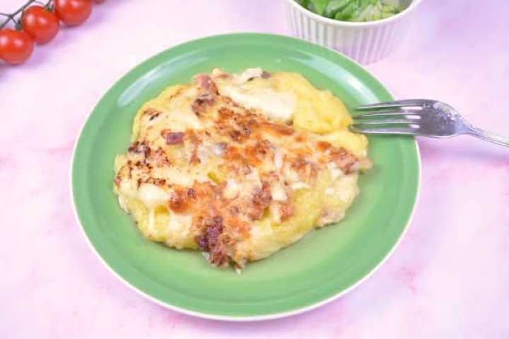 Served A square of layered baked cheesy polenta with bacon served on a green plate with fresh lettuce salad.