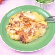 A warm portion of baked cheesy polenta casserole served on a plate with fresh butterhead salad.