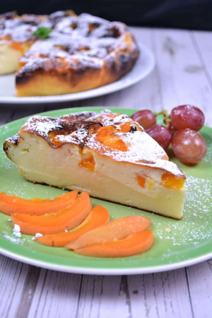 Serving A slice golden-brown gluten-free yoghurt cake served with sliced apricots and grapes on a green serving plate.