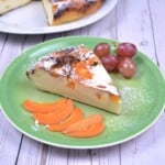 A slice golden-brown gluten-free yoghurt cake served with sliced apricots on a green serving plate.