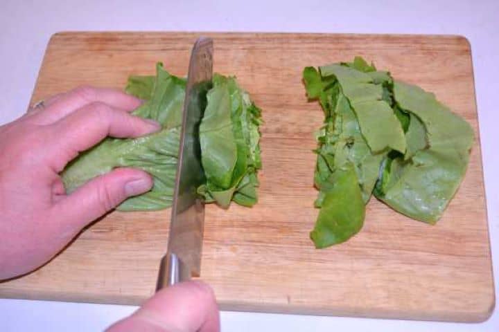 Cut Slicing fresh butterhead lettuce leaves into wide ribbons on a wooden chopping board.