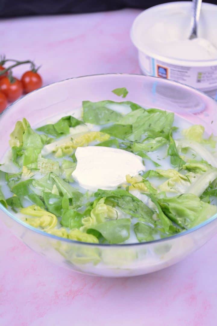 Serving Authentic Hungarian lettuce salad in a glass bowl topped with Greek yogurt and fresh dill.