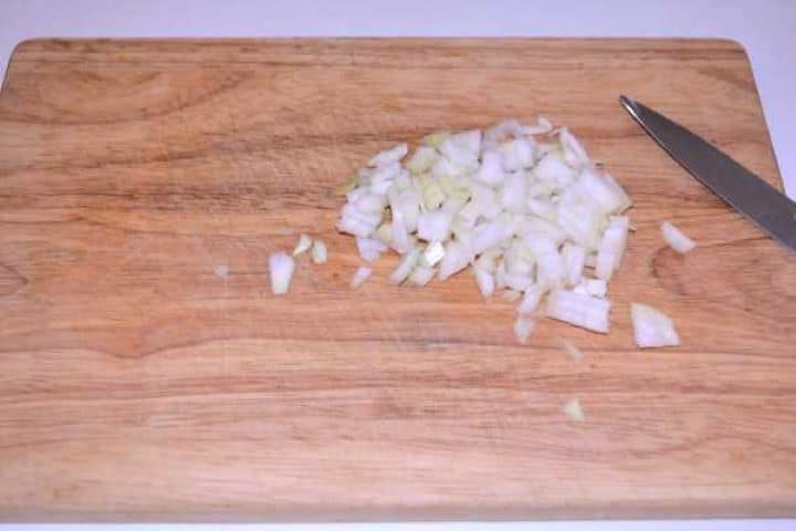 Onion Finely diced yellow onion on a wooden cutting board.