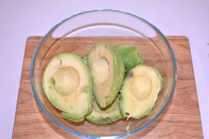 Avocados Freshly scooped ripe avocado halves in a glass mixing bowl.