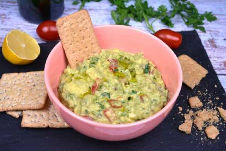 Serve Cilantro-free guacamole plated in a pink ceramic bowl with an assortment of crackers.