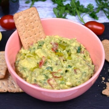Creamy guacamole without cilantro served in a pink bowl with crisp crackers.