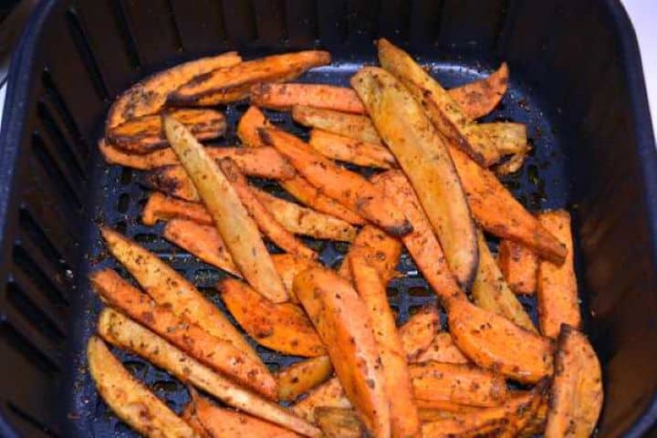 Fried Caramelized sweet potato wedges being shaken halfway through cooking in the air fryer basket to ensure even crispiness.