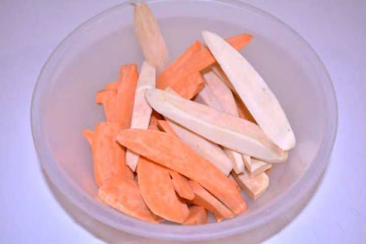 Wedges Raw peeled sweet potatoes being sliced into uniform 1.5 cm wedges in a bowl.