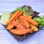 A plate of crispy golden-brown air fryer sweet potato wedges seasoned with sweet Hungarian paprika and served with fresh cucumber and lettuce.