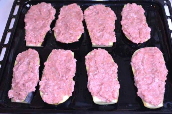 Layer Seasoned pork mince spread evenly across thick eggplant slabs on a baking sheet.