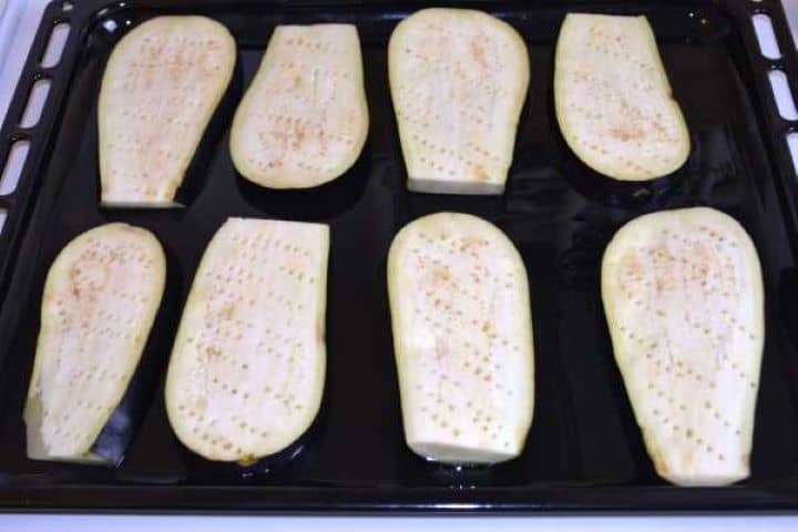 Eggplant slices arranged on an oiled baking tray and pierced with a fork to absorb cooking juices.