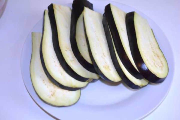 Eggplant Thick eggplant slices cut lengthwise on a white plate, ready for roasting.