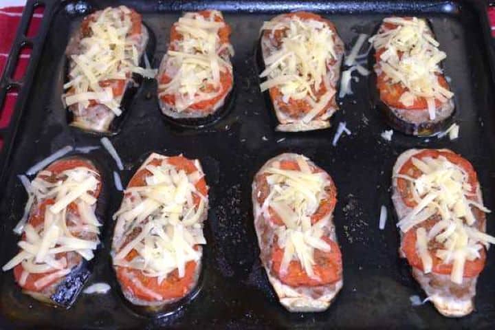 Roast Shredded cheddar cheese sprinkled over partially baked eggplant, meat, and tomato slices.