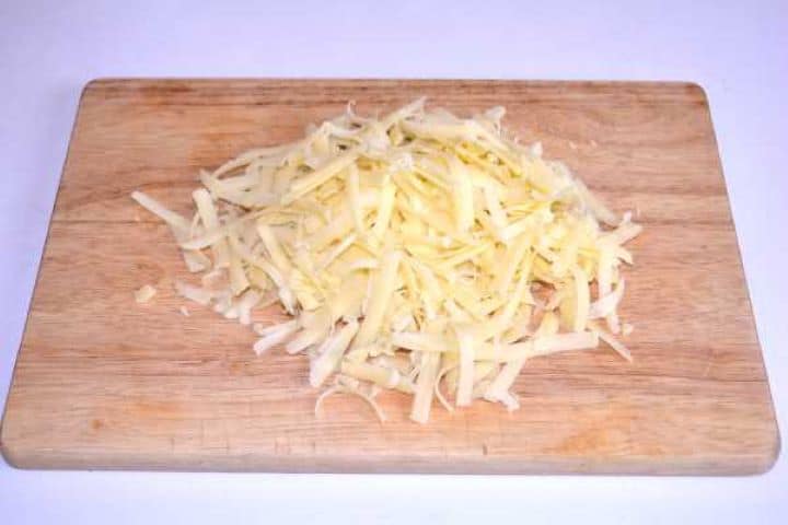Cheddar Freshly grated sharp cheddar cheese piled on a wooden cutting board.
