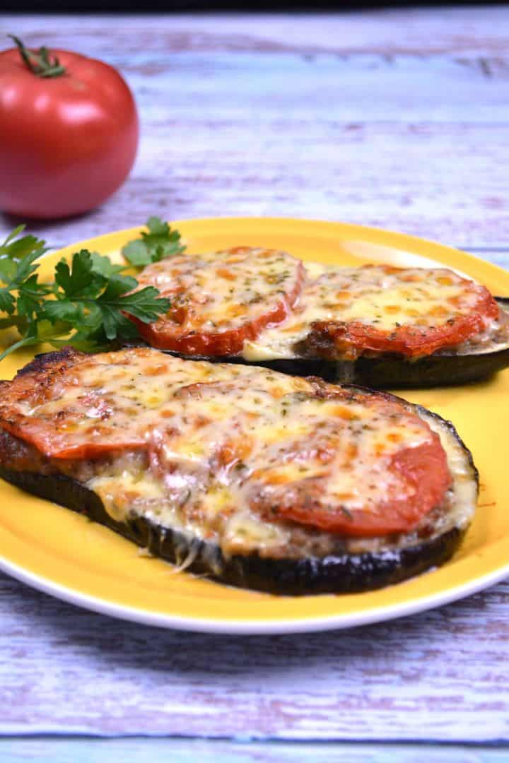 Serving Baked eggplant with minced pork topped with melted cheddar cheese and fresh tomatoes on a yellow plate.