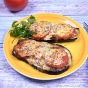 Baked eggplant with minced pork topped with melted cheddar cheese and fresh tomatoes on a yellow plate.
