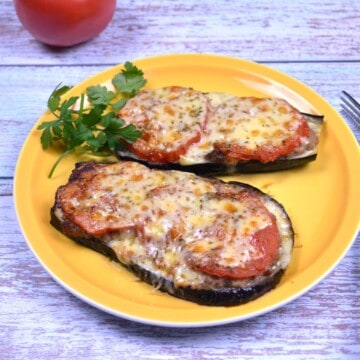 Baked eggplant with minced pork topped with melted cheddar cheese and fresh tomatoes on a yellow plate.
