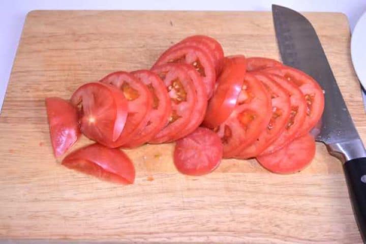 Tomatoes Thinly sliced ripe red tomatoes on a wooden chopping board.