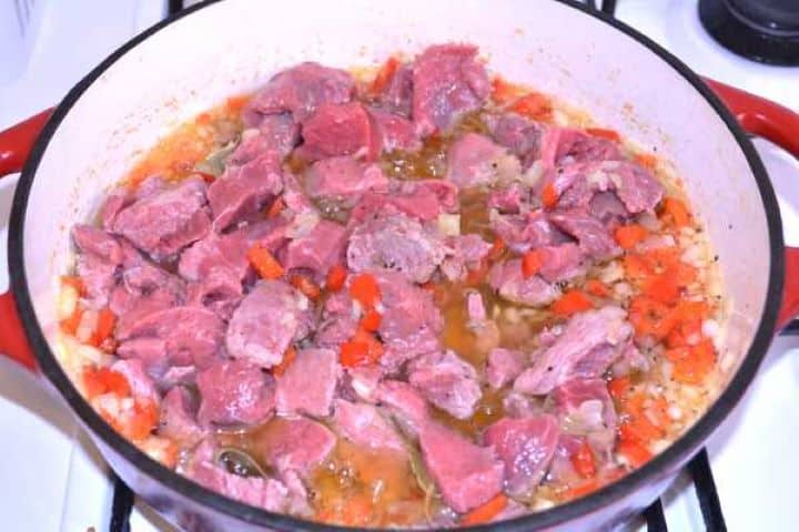 Beef Adding diced beef cubes to sautéed onions and peppers in a Dutch oven.