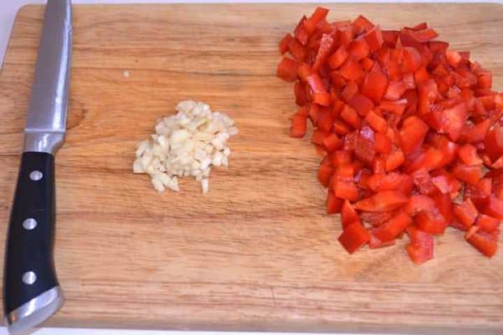 Chopped Bell Pepper Diced red bell pepper and minced garlic cloves on a cutting board.