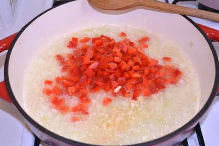 Bell Pepper Cooking chopped onions, red bell pepper, and garlic together in a Dutch oven.