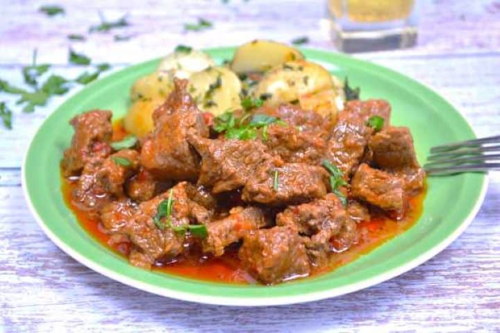 Serve Traditional Hungarian beef paprikash served with boiled potatoes on a green plate.